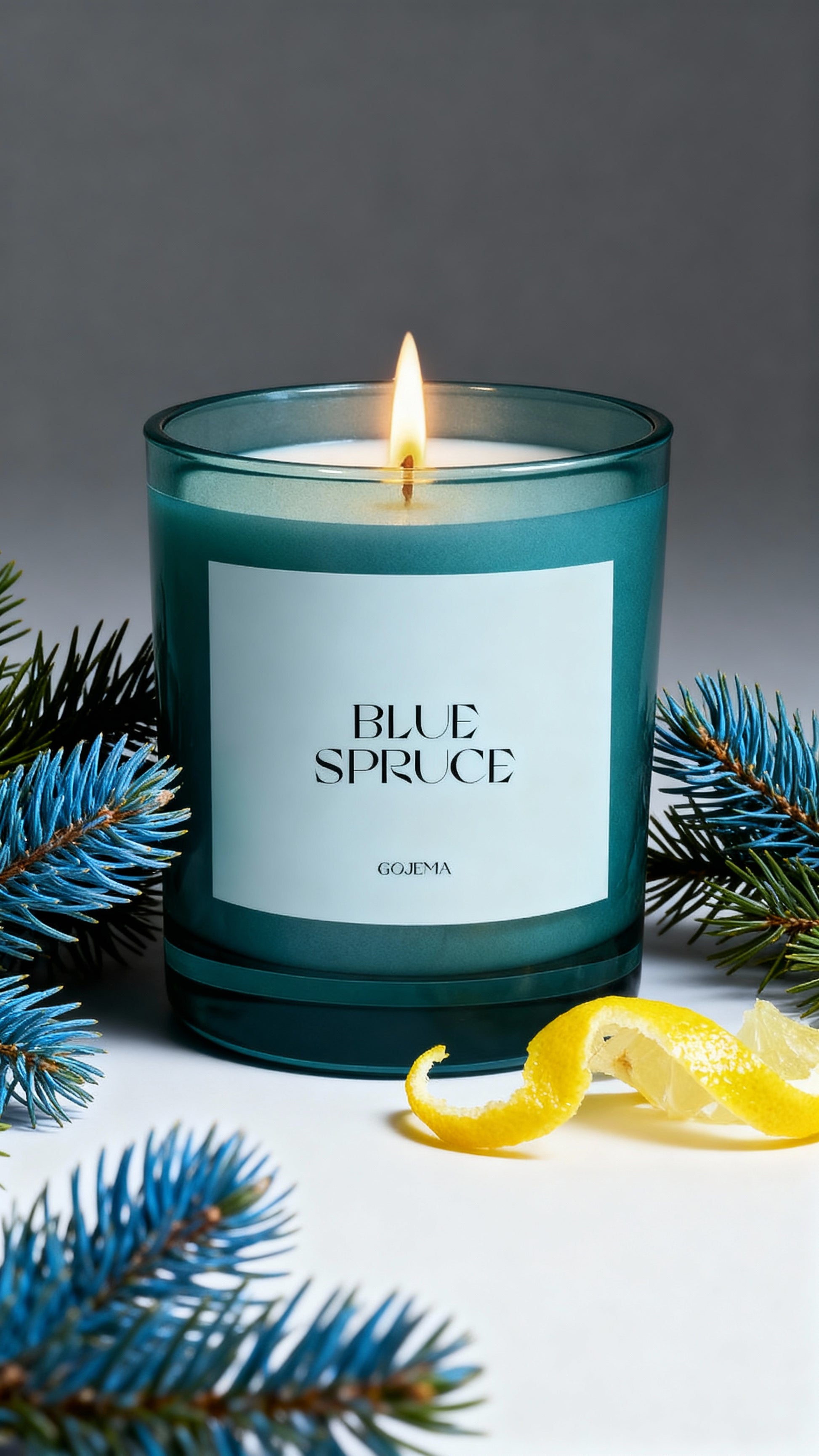 Candle labeled 'Blue Spruce' with evergreen branches and a lemon peel on a gray background