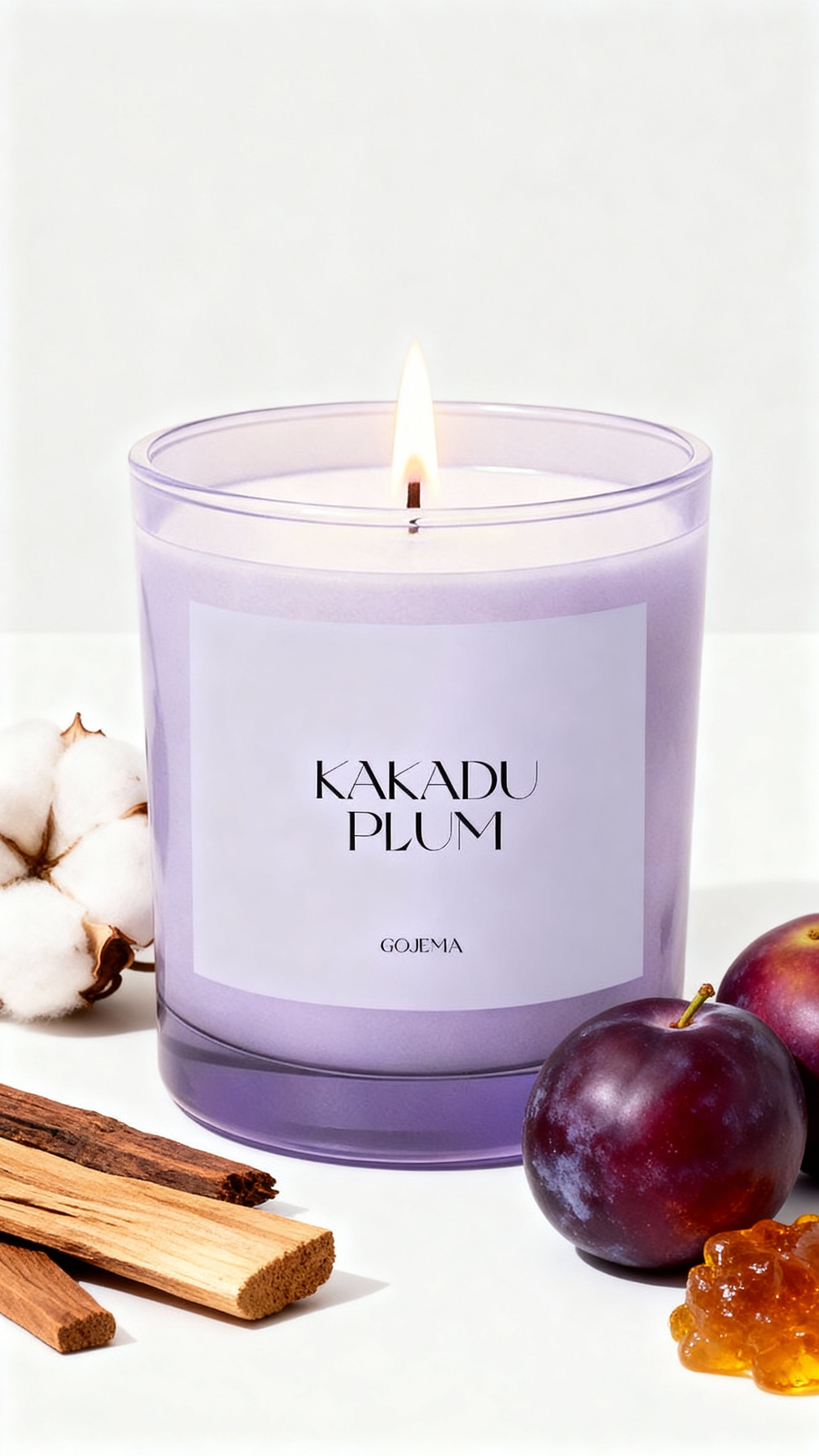 Candle labeled 'Kakadu Plum' with cotton, plums, and sandalwood on a white background