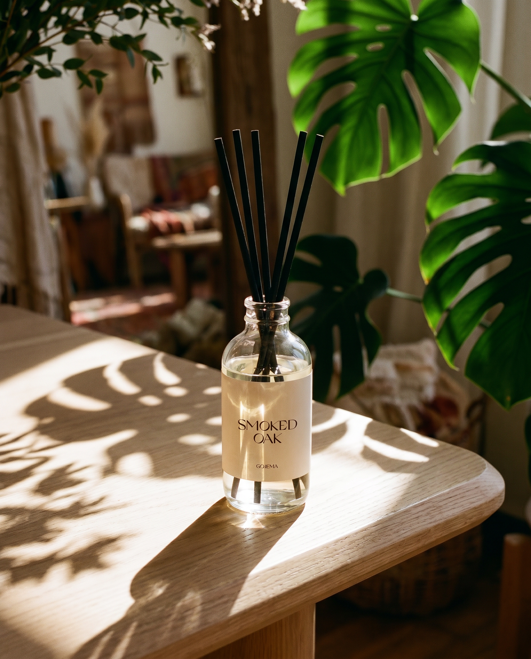 Diffuser bottle labeled 'Smoked Oak' on a wooden surface with plants in the background